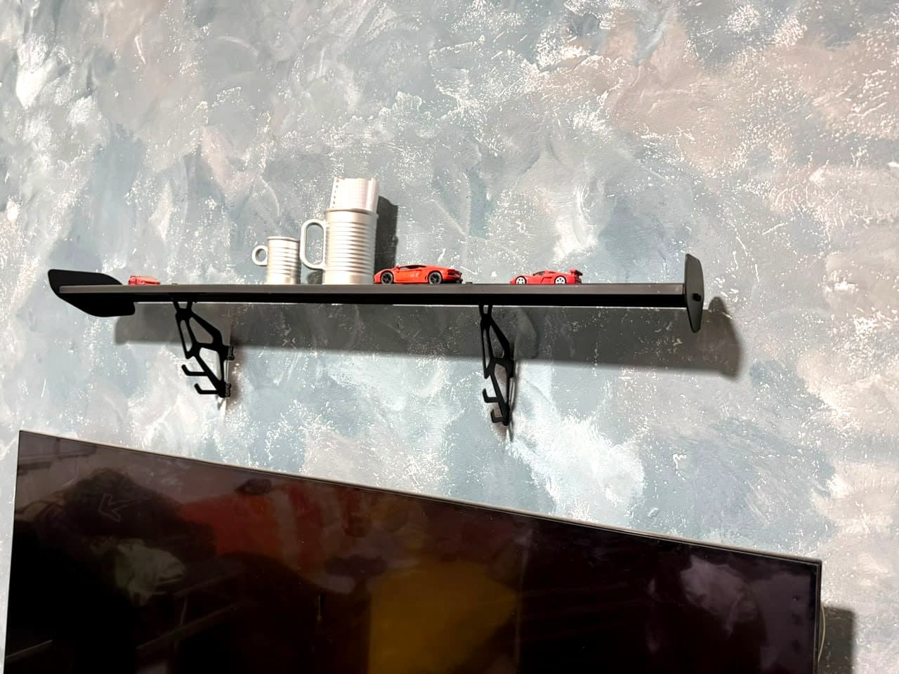 Le Spoiler Shelf fixé au mur, portant des tasses et des voitures miniatures